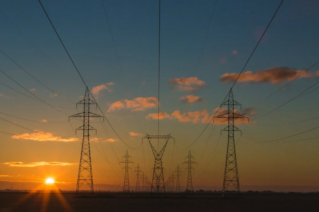 Hochspannungsmasten mit Stromleitungen vor einem Himmel bei Sonnenuntergang