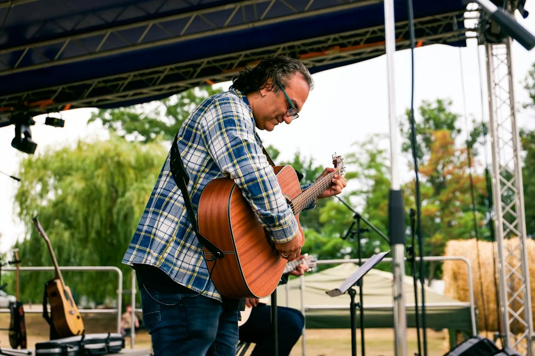 Musiker in kariertem Hemd spielt akustische Gitarre auf einer Bühne im Freien