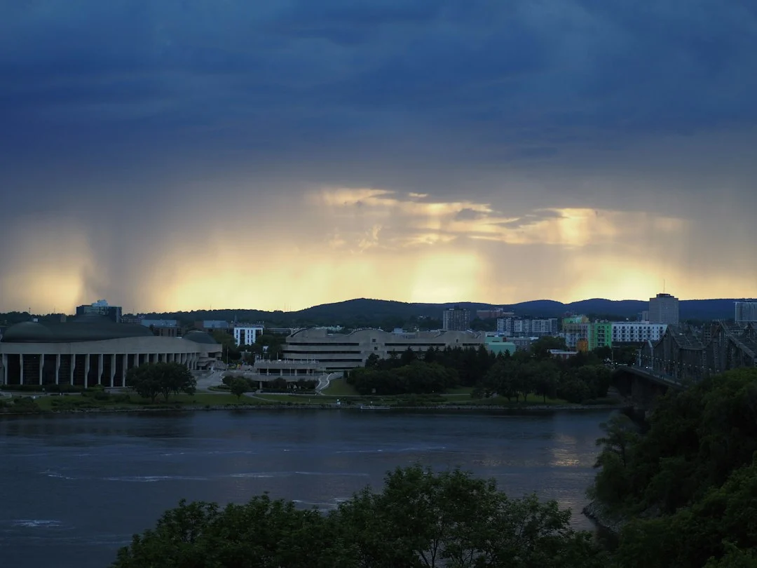 Regenschauer über einer Stadt am Flussufer bei dunklen Wolken