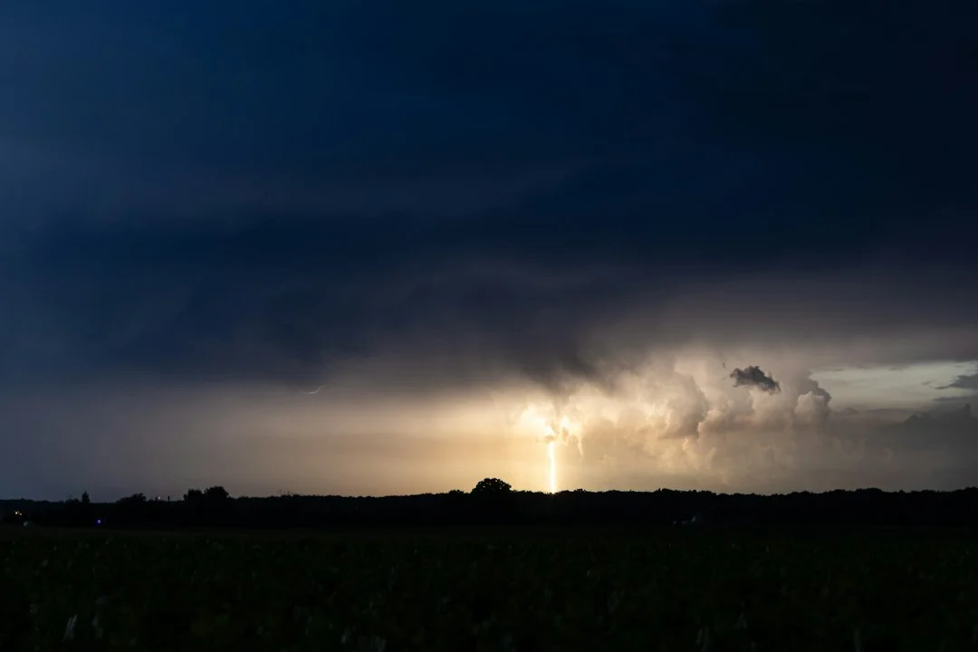 Blitzeinschlag aus dunklen Gewitterwolken über offenen Feldern