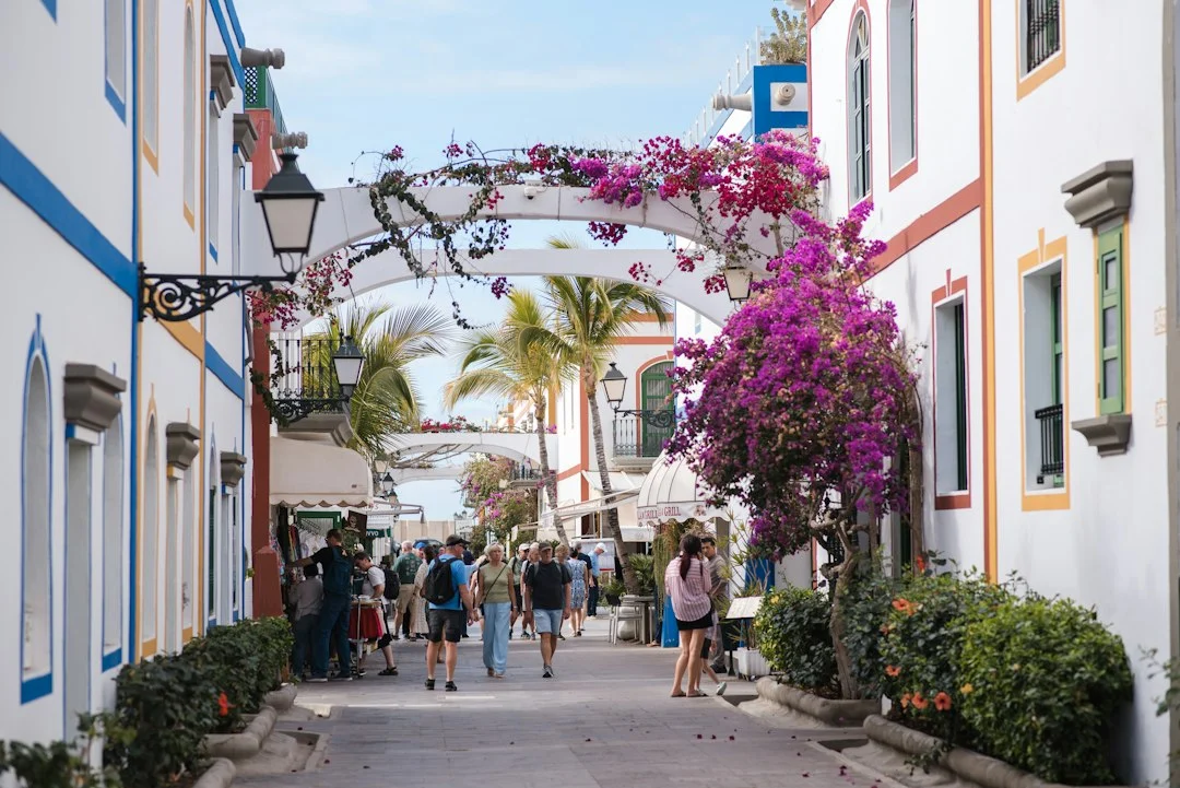 Menschen spazieren durch eine Fußgängerstraße mit weißen Häusern und blühenden Bougainvilleen